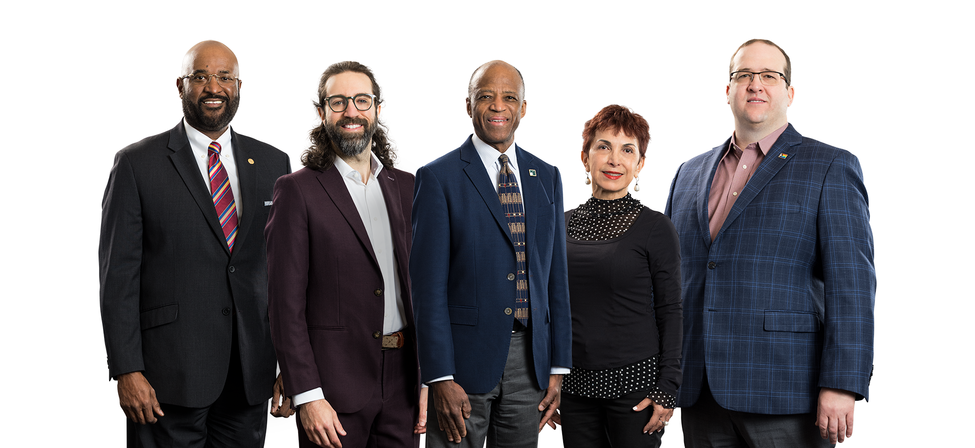 Five professionally dressed people stand in a row against a white background, smiling at the camera. The group includes three men in suits and ties, one man with long hair and glasses, and one woman in a black blouse.